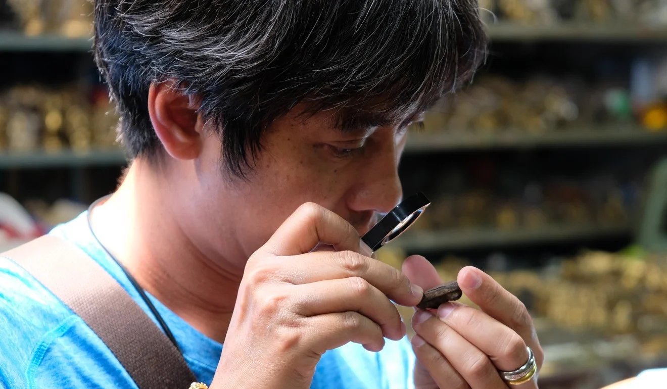 A customer scrutinises an amulet using a jeweller’s loupe